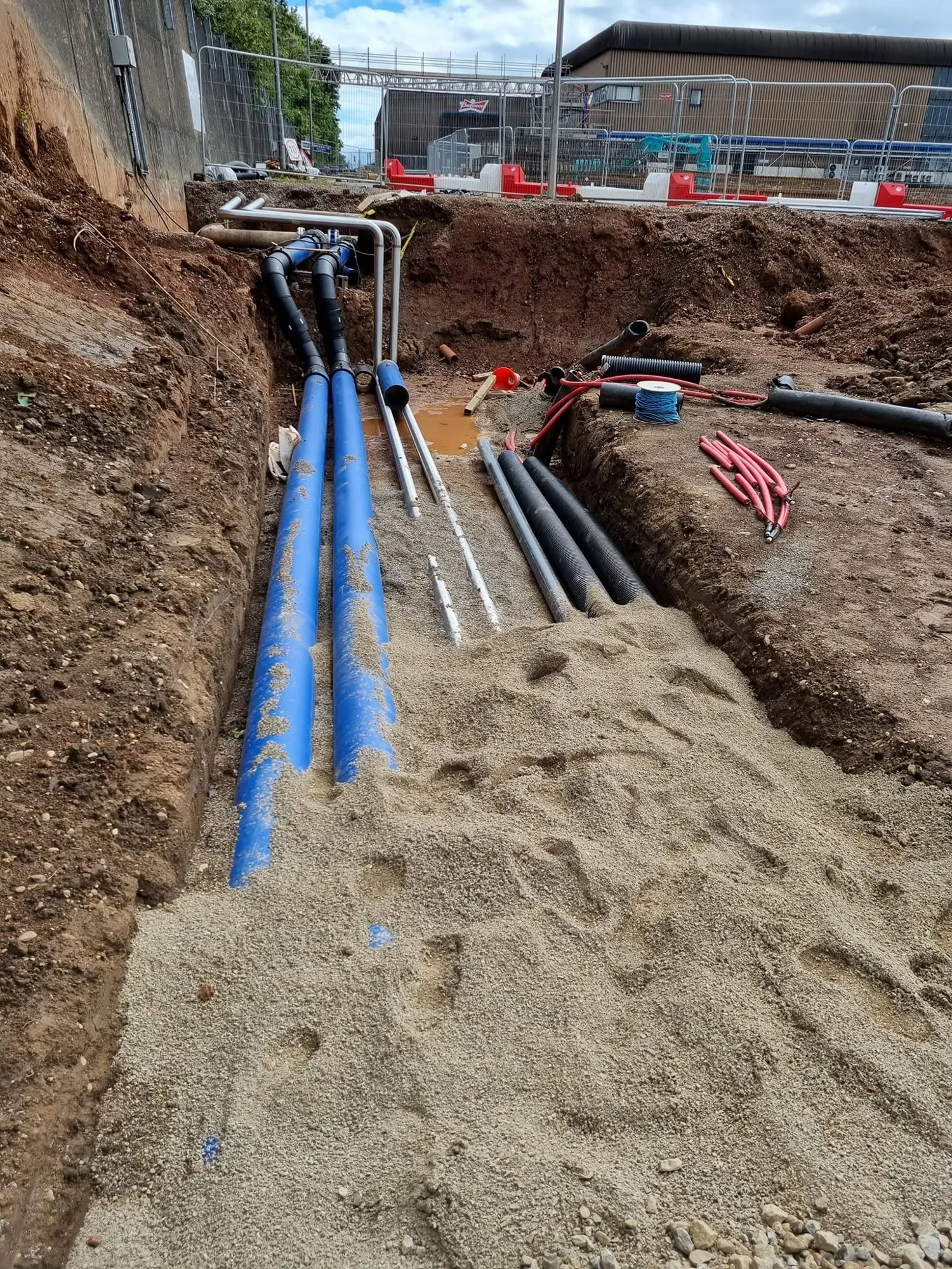 Blue water pipes and black ducts laid on a sand bed in a deep trench
