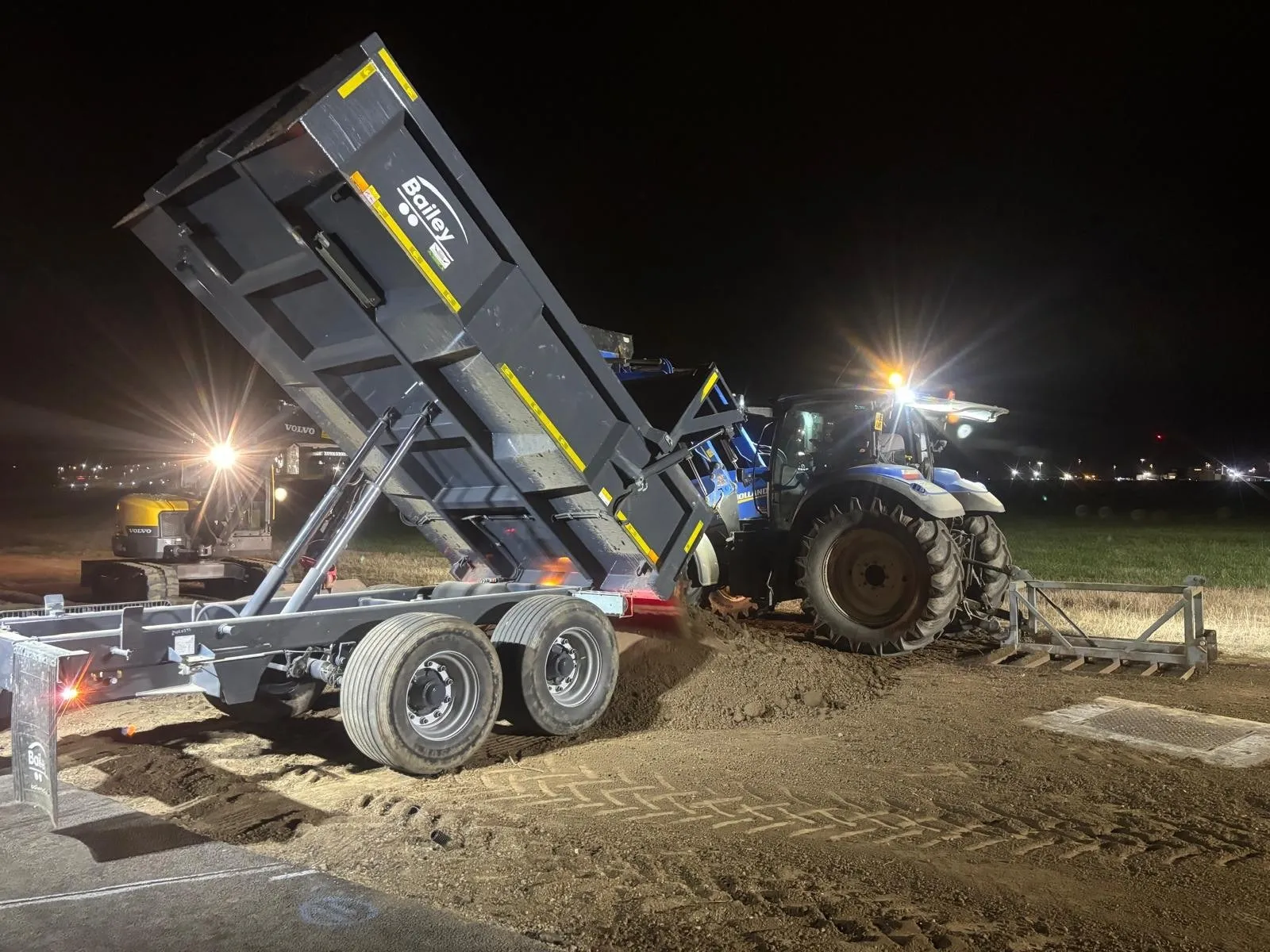 Tractor and tipping trailer delivering topsoil at night beside an airfield