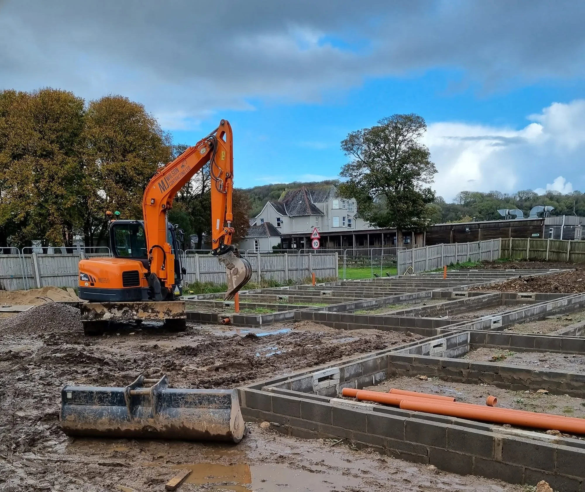 Excavator working among newly built foundation walls on a housing site