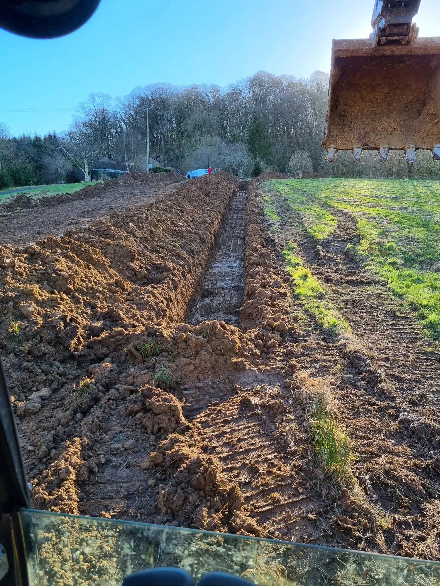 Excavator bucket cutting a land drain across pasture