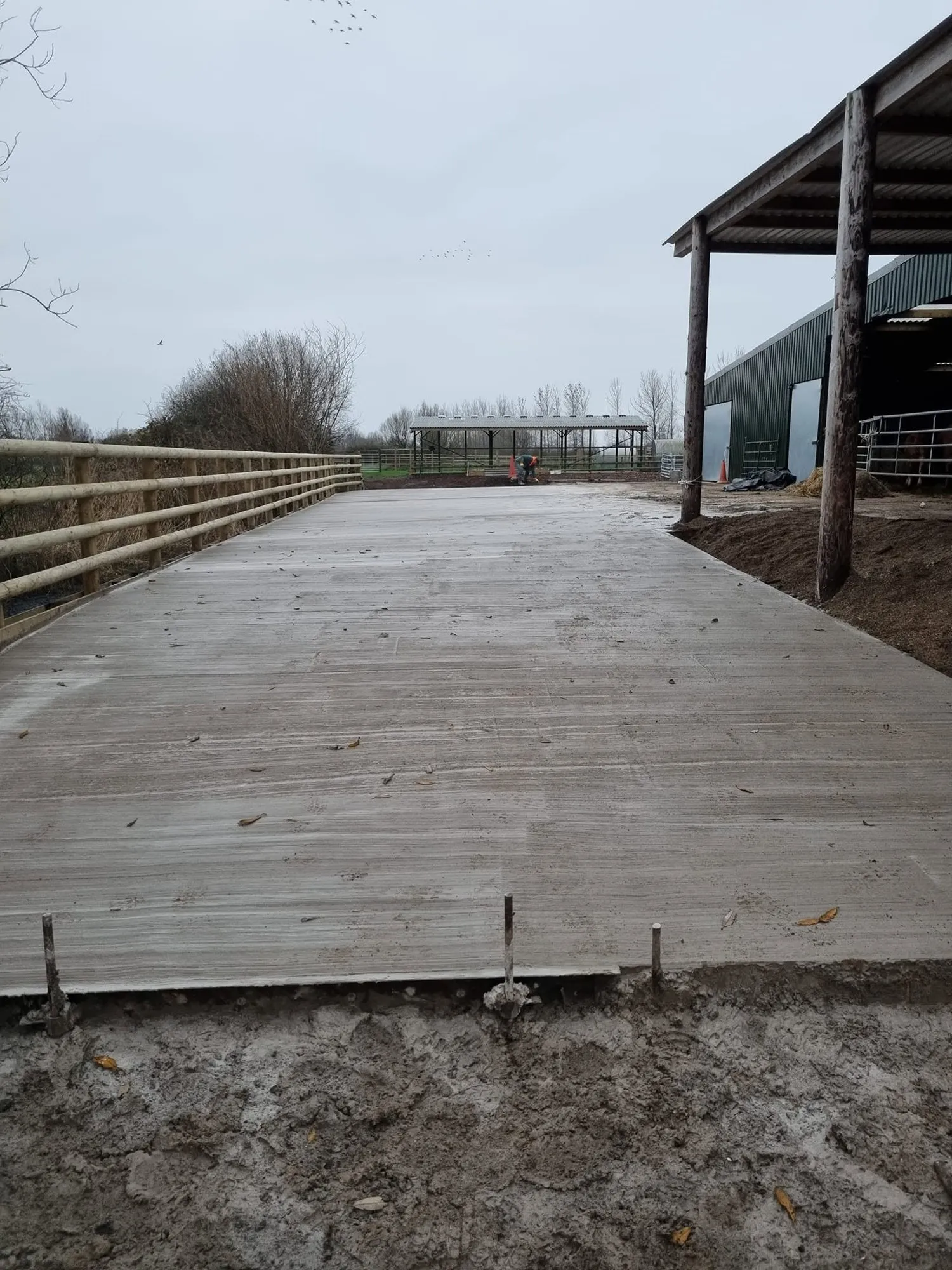 Freshly finished concrete yard beside a post and rail fence