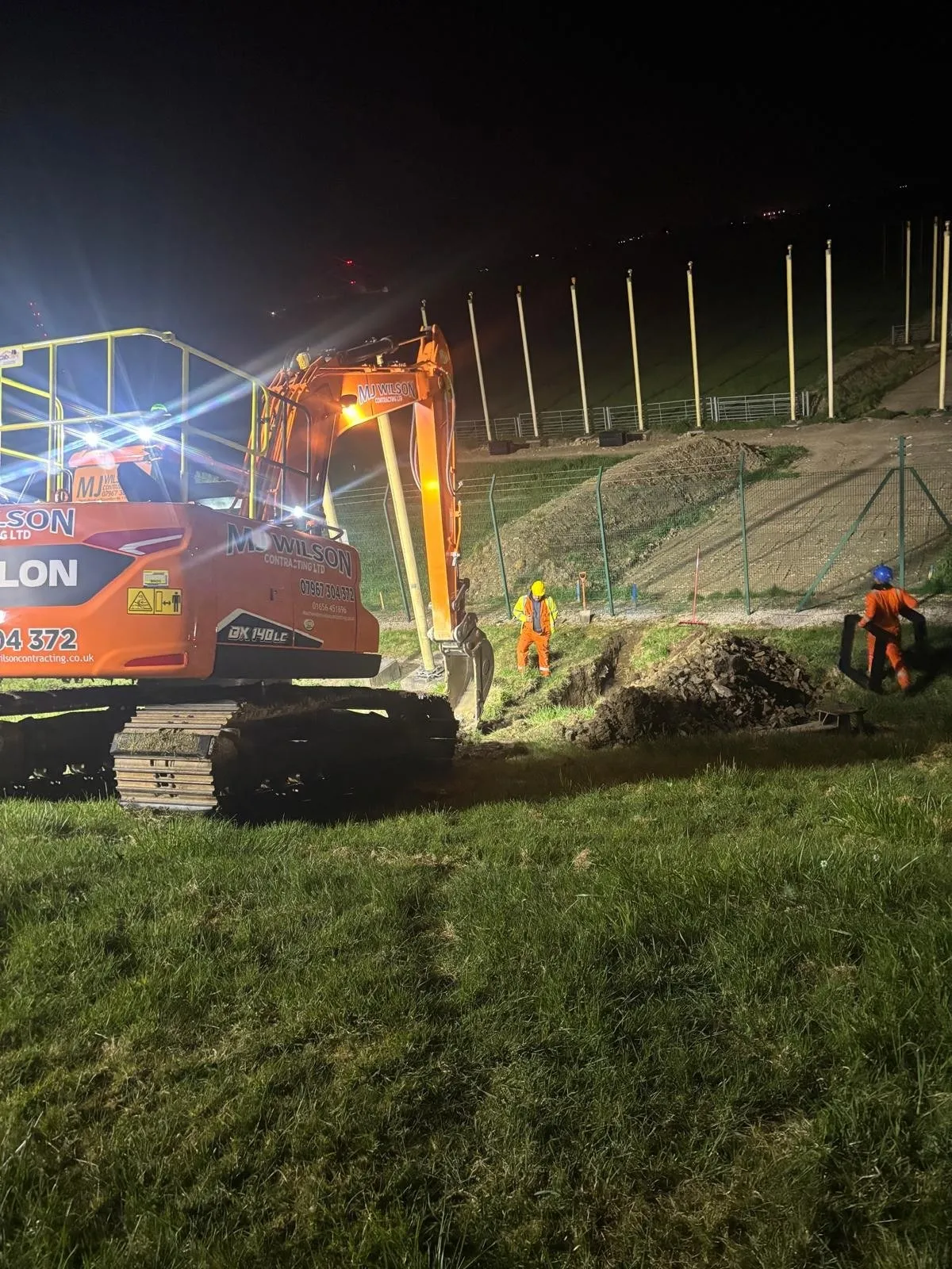 Excavator and crew working at night under lights