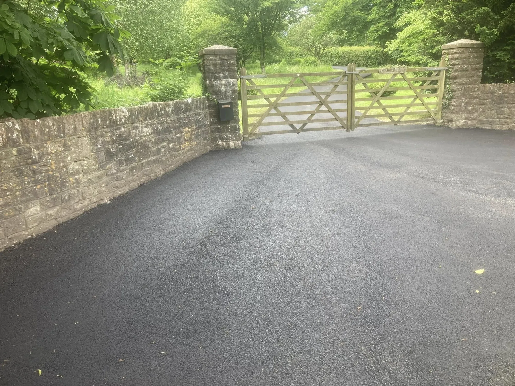 New tarmac surface at a stone-walled gateway with timber gates