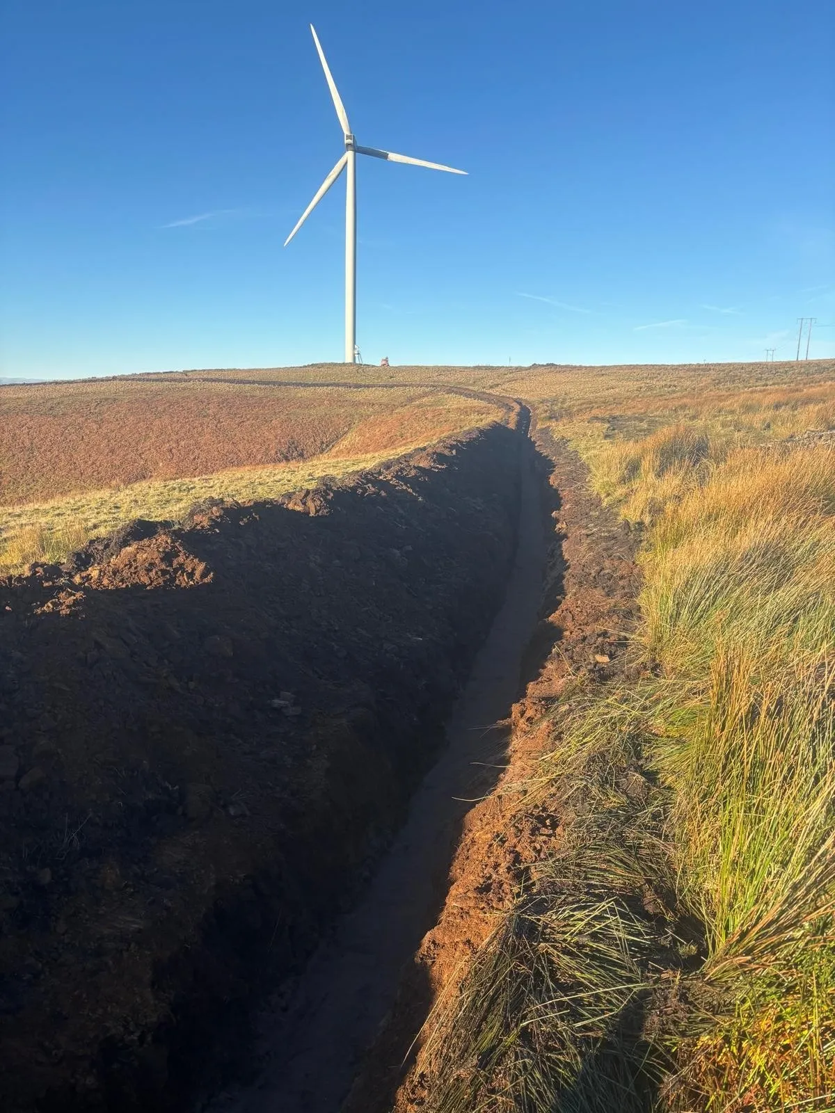 Cable trench cut through open ground with the route marked out