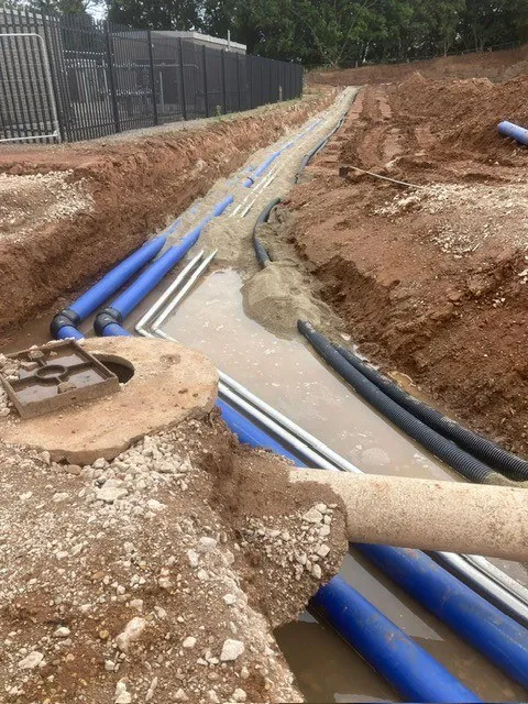 Blue service pipes in a sand-bedded trench by a fence