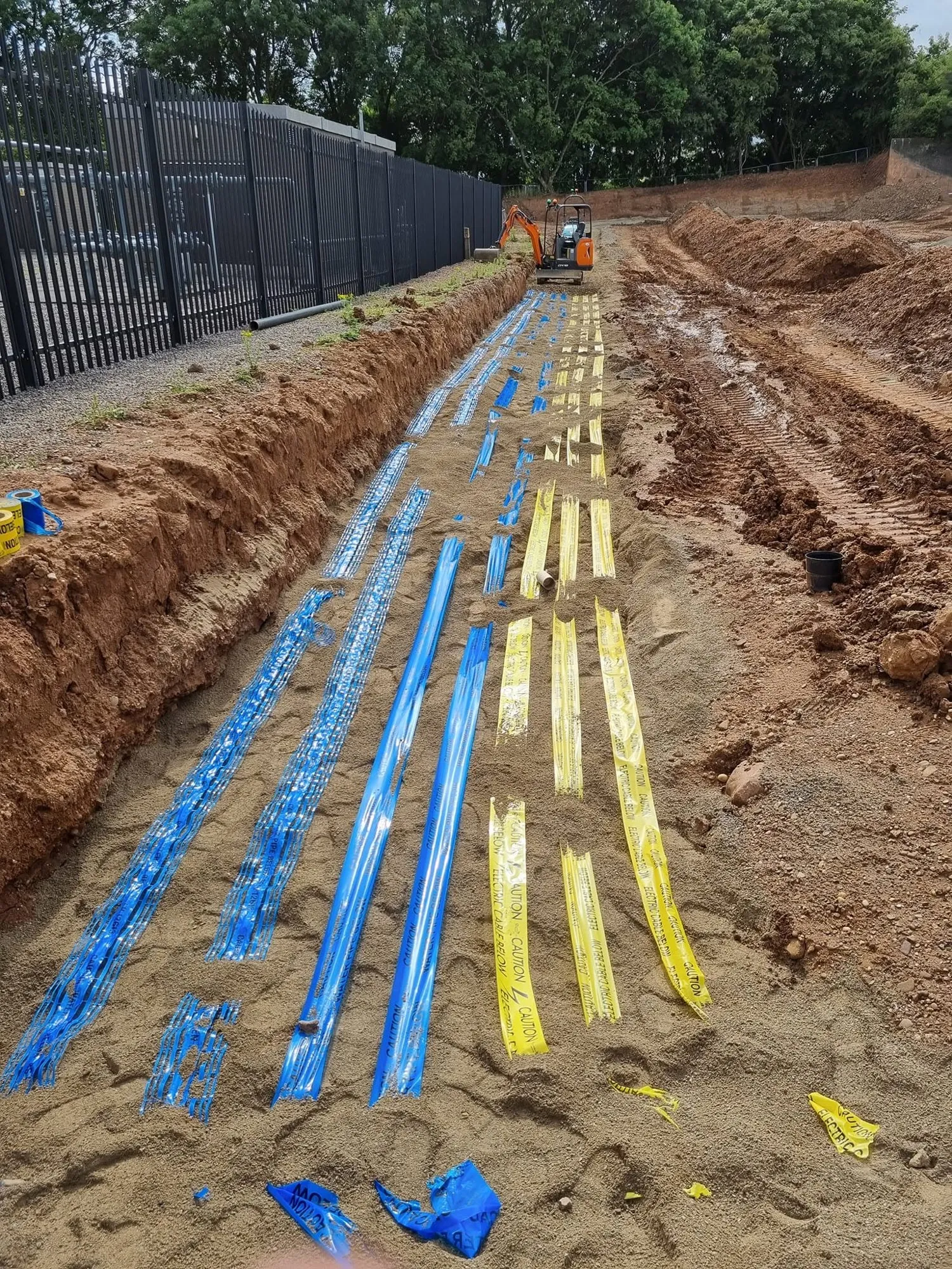 Warning tape laid over sand-covered services along a wide trench