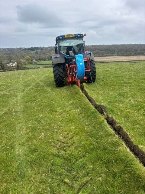 Tractor and trencher cutting a service trench across a field
