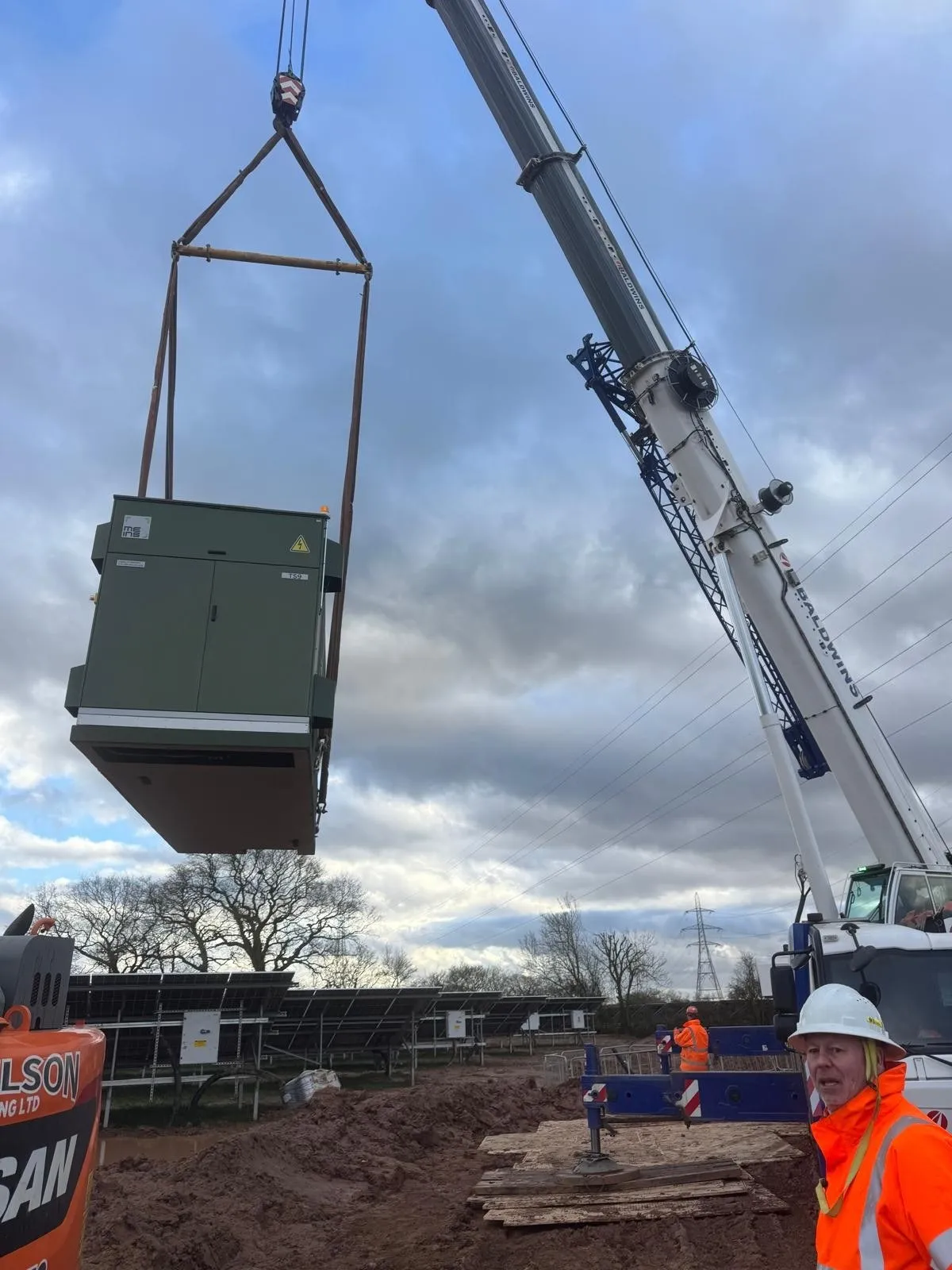 Crane lifting a substation unit into place beside solar panels