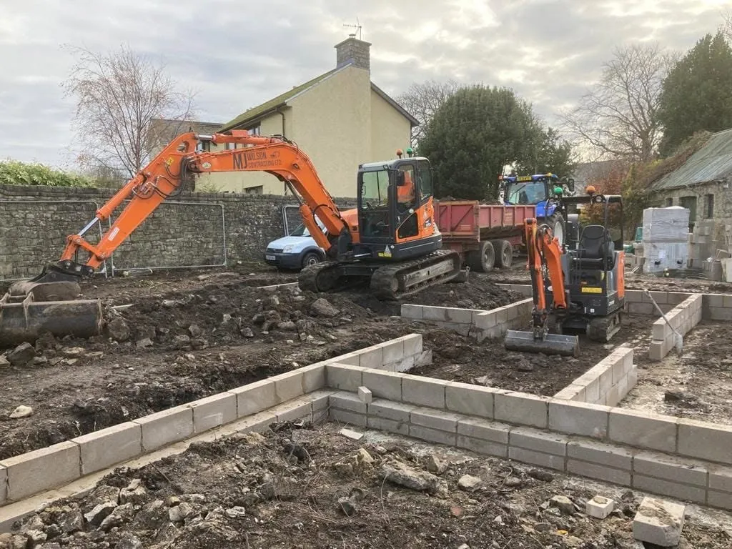 Two excavators working between blockwork foundation walls