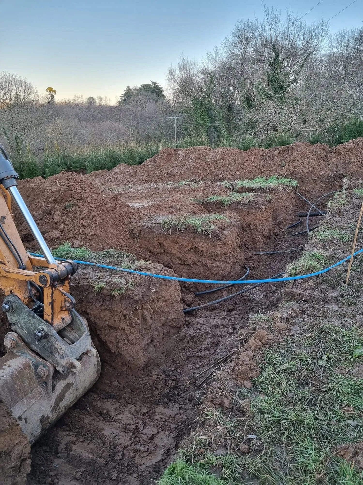 Excavator laying blue drainage pipe in a trench through a field