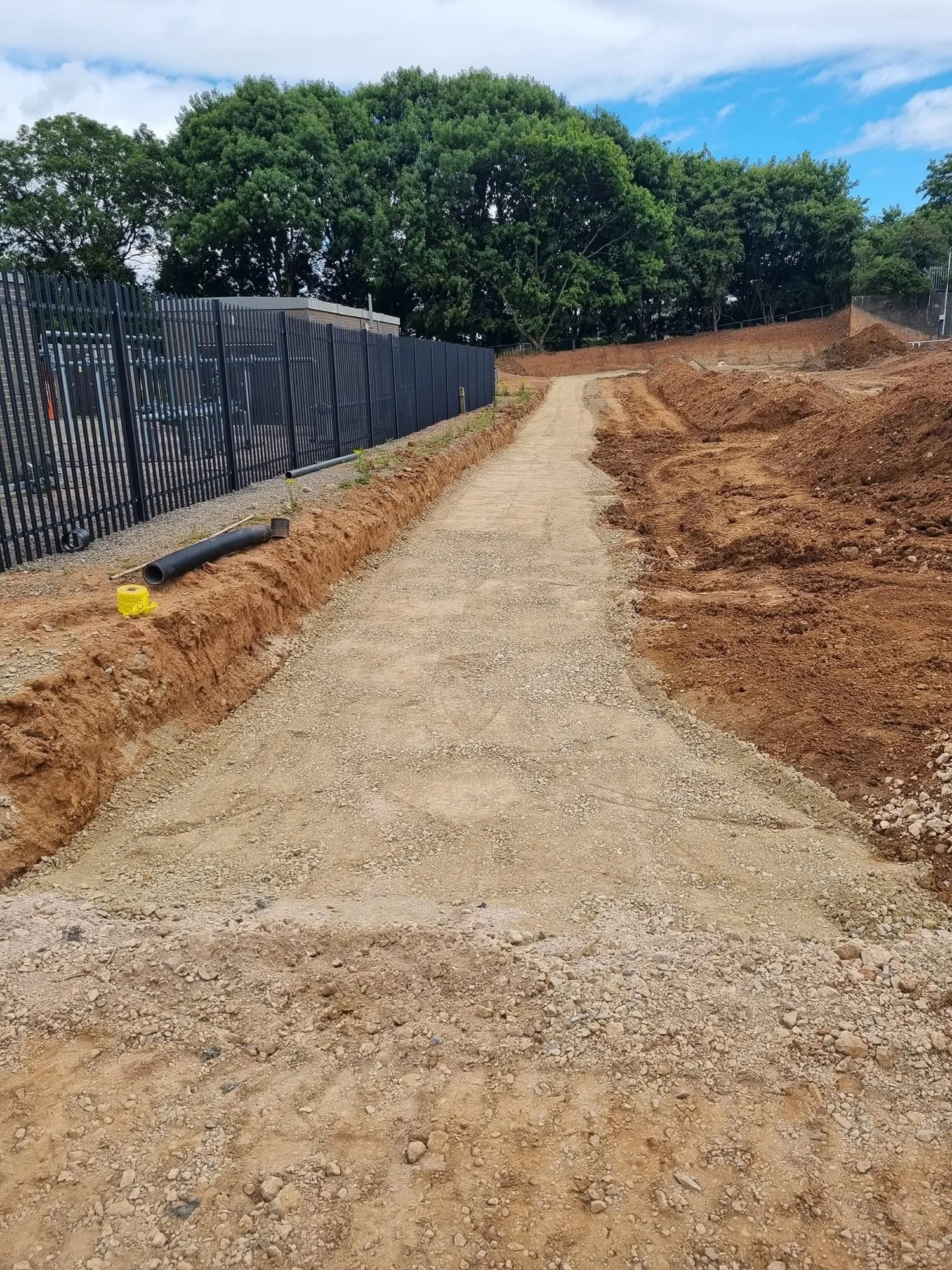 Compacted stone surface over the finished trench beside a security fence