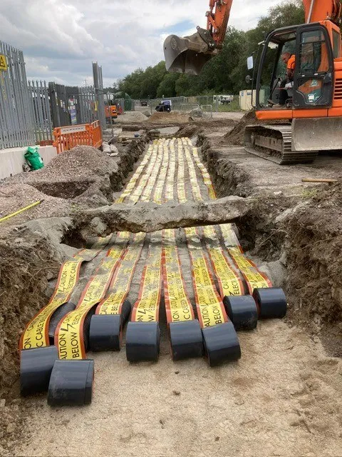 Multi-way ducts with electric cable warning tape laid in a trench beside an excavator