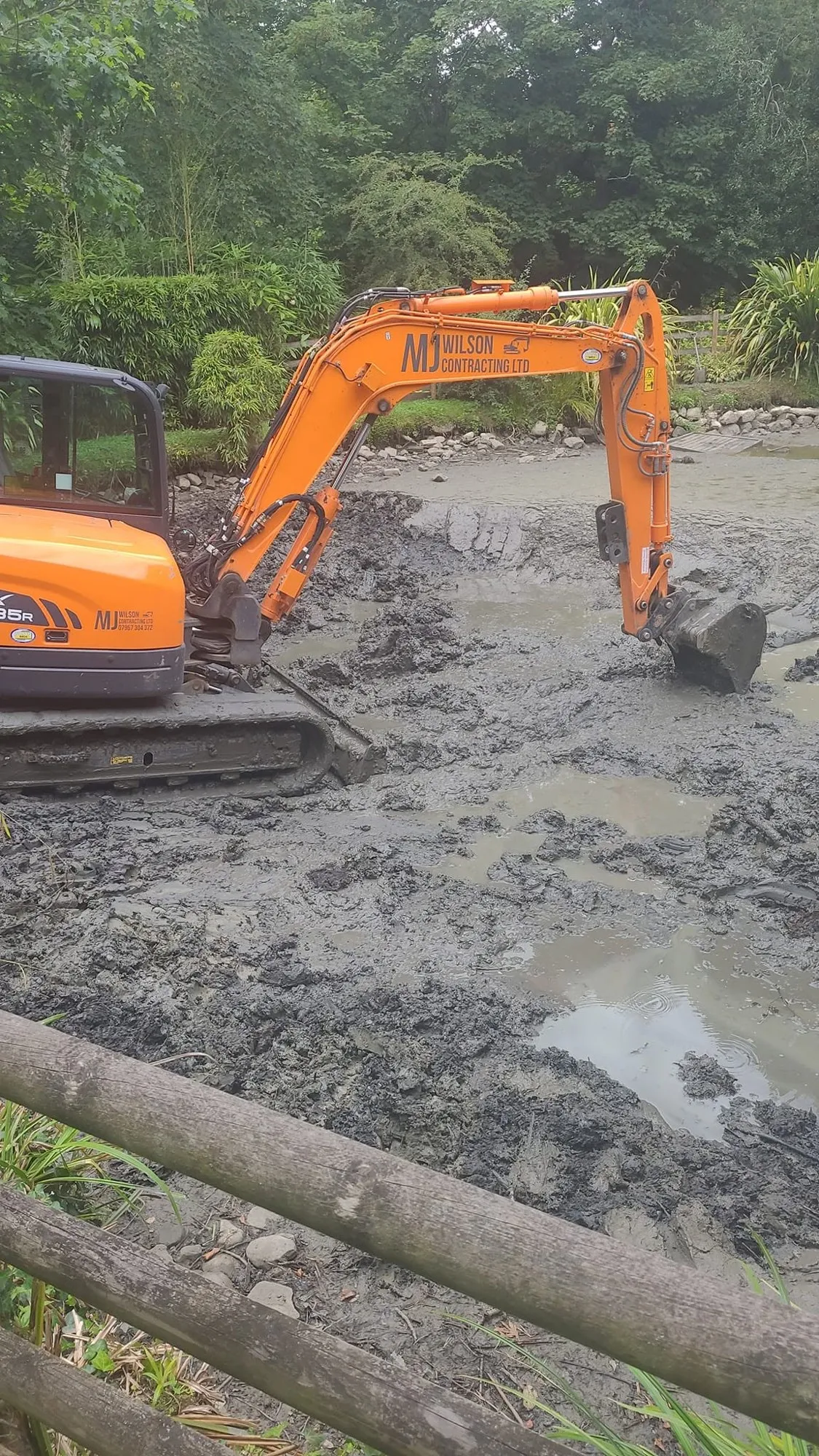 Excavator digging out deep silt from the pond bed