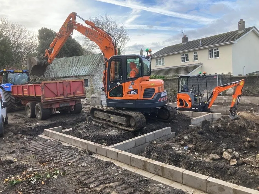 Excavator loading a tractor and trailer beside new footings