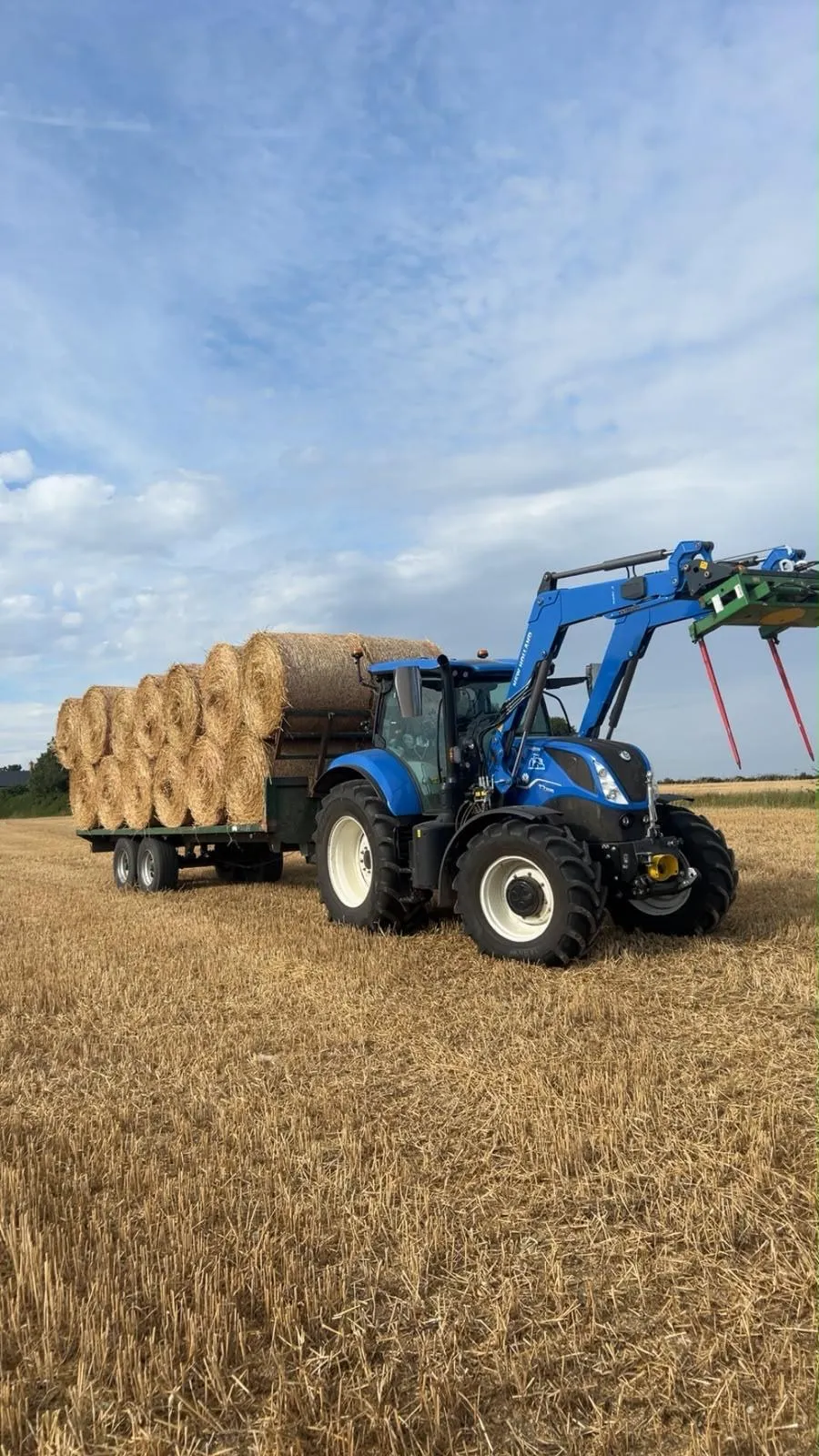 Tractor and loader with a trailer of round straw bales on a stubble field