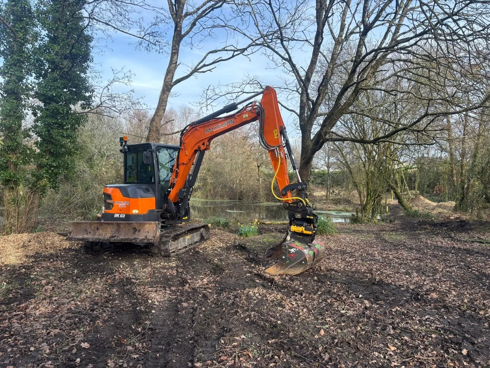 Excavator with a tilting bucket grading the bank beside a pond